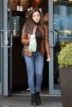 a woman walking out of a building with her hand in her pocket and holding a starbucks bag