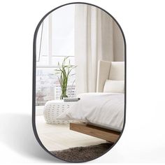 an oval mirror reflecting a bedroom with a bed in the foreground and a potted plant behind it