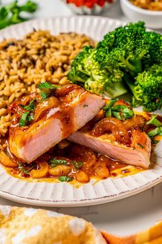 a white plate topped with meat covered in sauce next to broccoli and rice