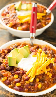 two bowls filled with chili, cheese and avocado on top of a wooden table