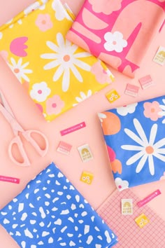 several different types of fabric and scissors on a pink surface with flowers, hearts, and dots