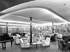 an old black and white photo of people in a library with piano, chairs, and bookshelves