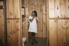 a woman standing in a bathroom next to a toilet and wooden paneling on the walls