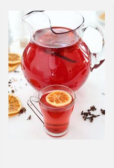 a pitcher of red liquid next to a cup filled with tea and sliced oranges