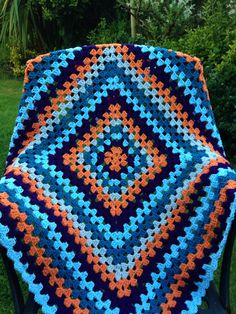 a crocheted granny blanket sitting on top of a chair in the grass next to a tree