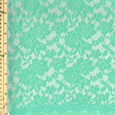 green lace fabric with flowers and leaves on the side, in front of a ruler