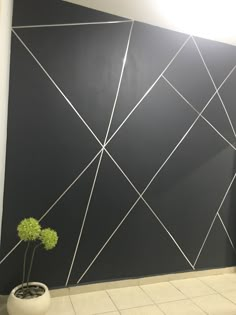 a white vase with a green plant sitting in front of a black and white wall