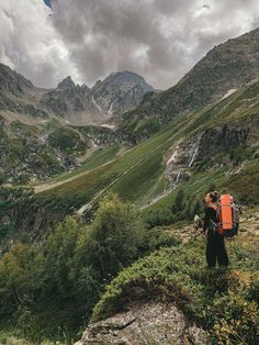 a person with a backpack standing on top of a mountain looking at the valley below