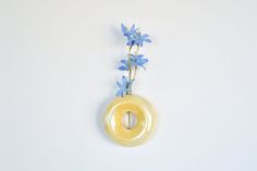 a yellow vase with blue flowers in it hanging from the wall on a white wall