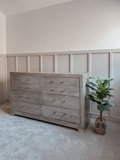 an empty room with a dresser and potted plant