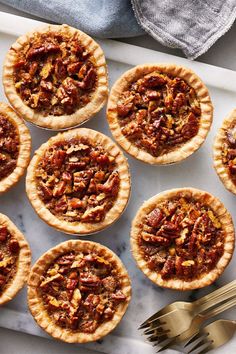 small pecan pies on a tray with whipped cream and forks next to them