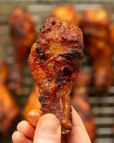 a hand holding up a piece of food in front of some chicken wings on a grill