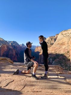 two people sitting on the edge of a cliff