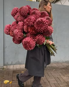 a woman is walking down the street carrying large bunches of flowers on her back