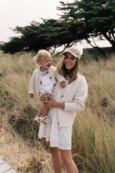 a woman holding a small child in her arms while standing next to tall grass and trees