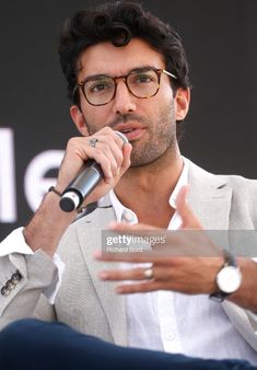 a man with glasses talking into a microphone while wearing a white shirt and gray jacket