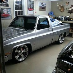 a silver truck parked in a garage next to other cars and deer heads on the wall