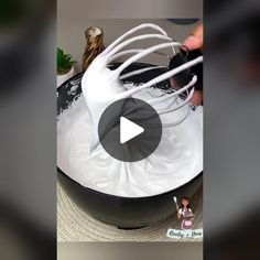 a person mixing white batter in a black bowl with a whisk on top