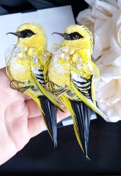 two small yellow birds sitting on top of each other's hands next to flowers