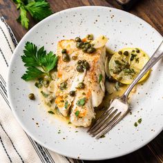 a white plate topped with fish covered in sauce and garnished with lemon wedges