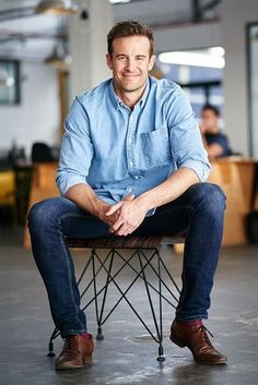 a man sitting on top of a wooden chair in an office building with people working behind him