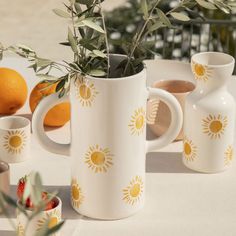 a table topped with white vases filled with oranges and greenery next to each other