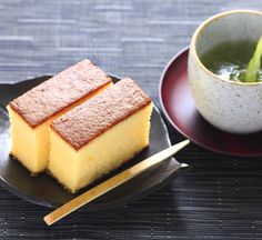 two pieces of yellow cake on a plate next to a cup of green tea and chopsticks