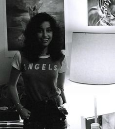 black and white photograph of a woman standing in front of a lamp with an angel t - shirt on