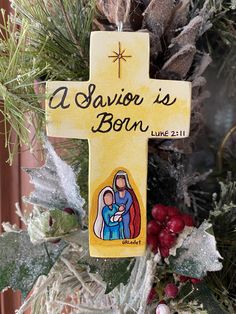 a wooden cross hanging from the side of a christmas tree with a nativity sign on it