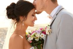 a bride and groom kissing on the beach with flowers in front of their heads,