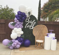 a balloon arch with purple, white and lavender balloons on it next to a wicker chair