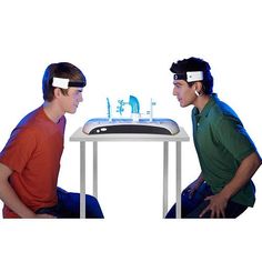 two young men sitting at a table with an electronic device in front of their faces