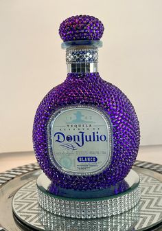 a bottle of tequila sitting on top of a glass plate covered in purple beads and crystals