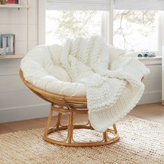 a wicker rocking chair with a white blanket on it in front of a window