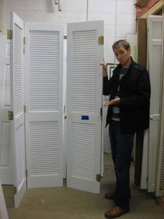 a woman standing in front of two white doors with shutters on each side and one open