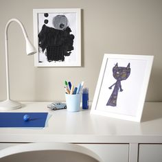 a white desk topped with a lamp next to a painting and pencils on top of it