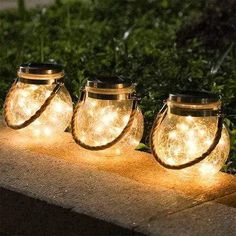 three mason jars with fairy lights are sitting on the ground in front of some bushes