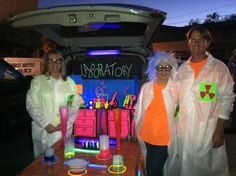 three people dressed in lab coats standing next to a table with neon items on it