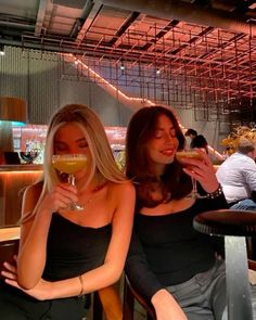 two women sitting next to each other at a table with drinks in front of them