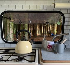 a tea kettle sitting on top of a stove next to a cup and coffee mug