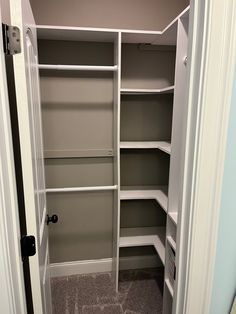 an empty walk in closet with white shelving and gray carpeted flooring is shown