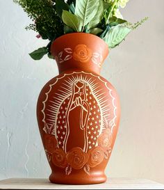 a vase with flowers in it sitting on a table next to a white wall and green leaves