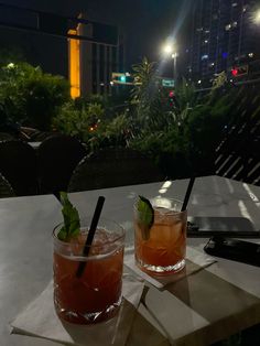 two cocktails sitting on top of a table next to each other in front of a cityscape