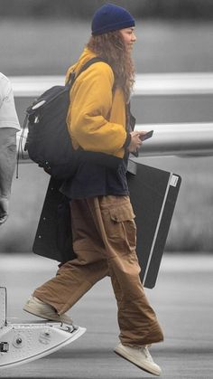 a man with long hair and beard carrying luggage while walking down the street next to an airplane