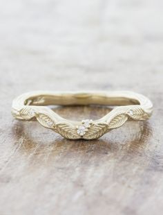 a gold wedding band with two diamonds on the top and bottom, sitting on a wooden surface