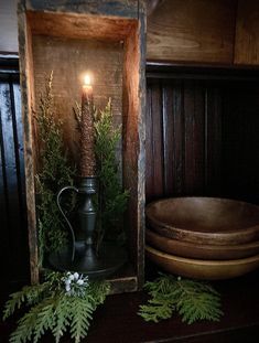 a candle is lit in a wooden box with greenery on the shelf next to it