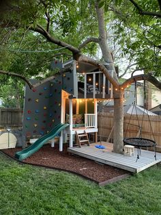 a backyard with a tree, swing set and climbing wall in the back yard area