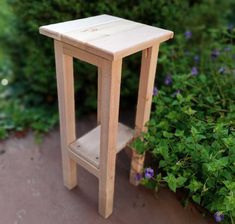 a small wooden table sitting in front of some bushes and flowers on the ground with purple flowers around it