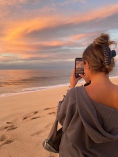 a woman taking a photo with her cell phone on the beach at sunset or sunrise