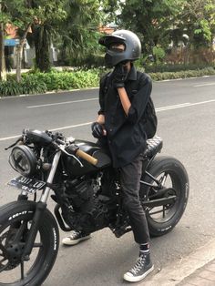 a person sitting on a motorcycle with a helmet and jacket over their shoulders, talking on the phone